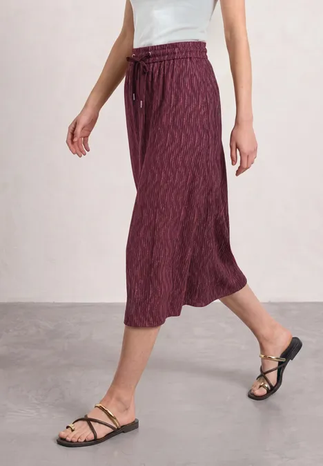 Midirock mit Elastikbund und Print blush berry Frau im bordeauxfarbenen Midi-Rock mit Wellenmuster und schwarzen Riemchensandalen.