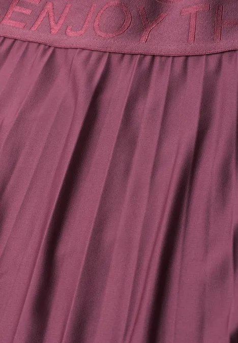 Jupe midi à structure plissée dark clouded blush Gros plan sur une jupe plissée bordeaux à taille élastiquée ornée d’un lettrage
