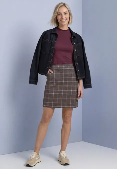 Knielanger Veloursrock mit Karomuster silk brown Eine Frau trägt eine Jeansjacke, burgunderfarbenen Pullover, karierten Rock und bequeme Sneaker.