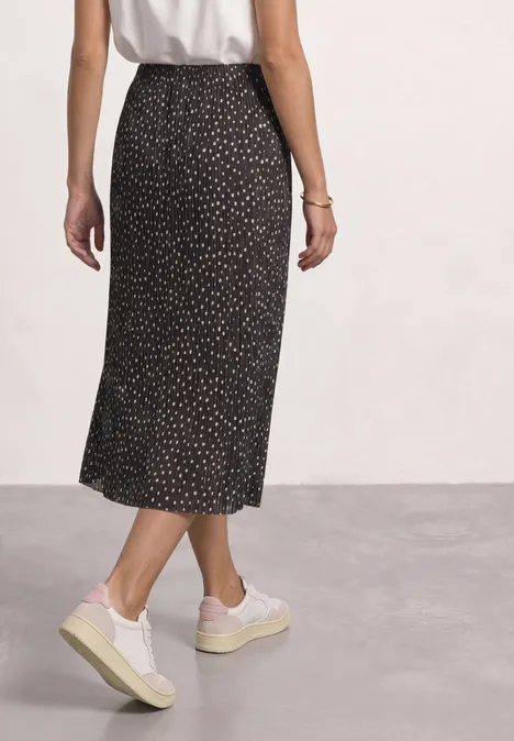 Midirock aus Mesh in Plisséestruktur black coffee Frau von hinten in weißem Top, schwarzem Midirock mit dezentem Muster und weißen Plateau-Sneakern.