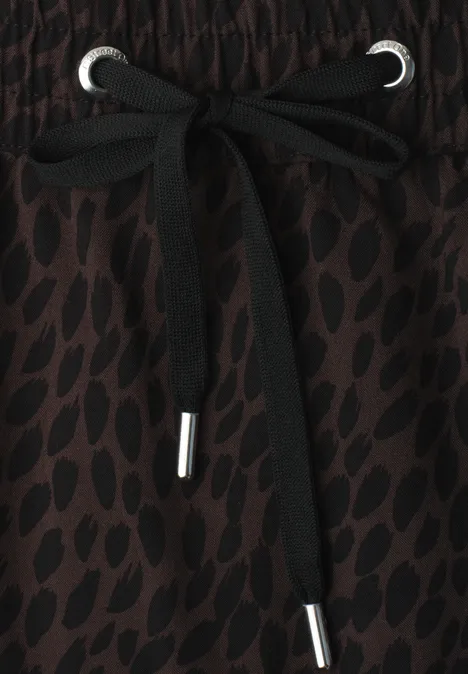 Gros plan sur un cordon noir à embouts métalliques sur un tissu marron à motifs.