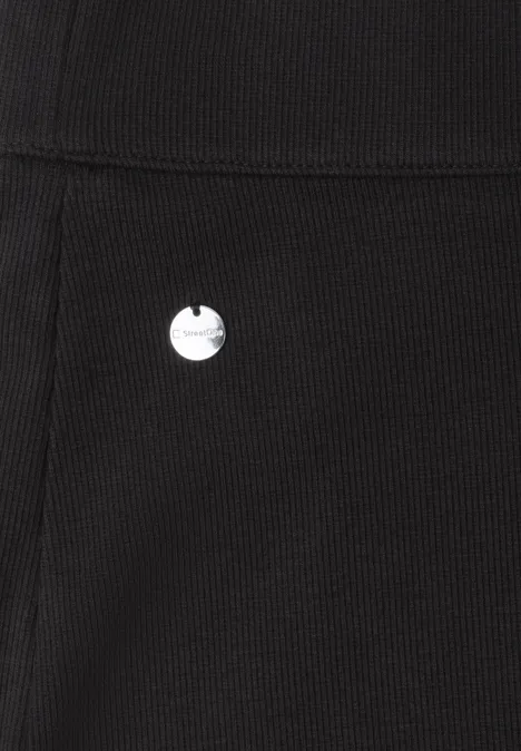 Gros plan sur un tissu noir côtelé avec un petit emblème métallique rond.