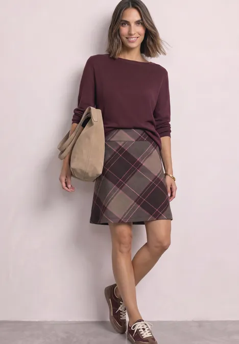 Minirock mit Karomuster rustic rouge Frau trägt burgunderfarbenen Pullover, karierten Rock und beige Umhängetasche.