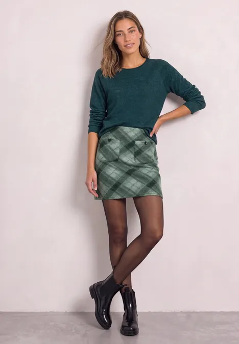 Knielanger Rock mit Patch-Pockets stormy green Frau mit grünem Pullover, karriertem Minirock, schwarzen Strumpfhosen und Boots vor hellem Hintergrund.
