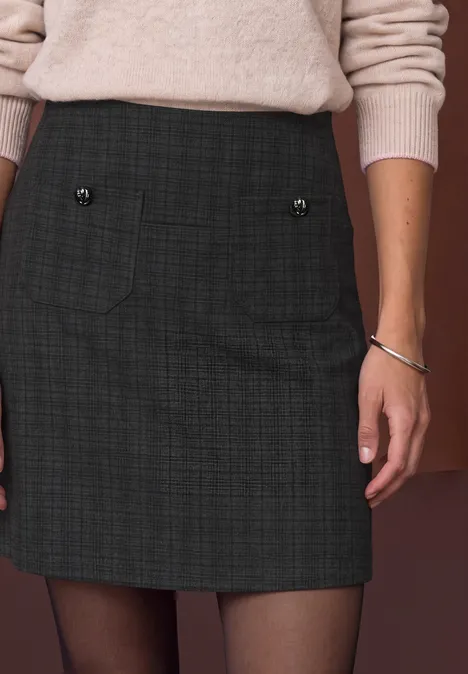Frau trägt knapp über dem Knie sitzenden, karierten Minirock mit Taschen und Knöpfen, kombiniert mit hellem Pullover.