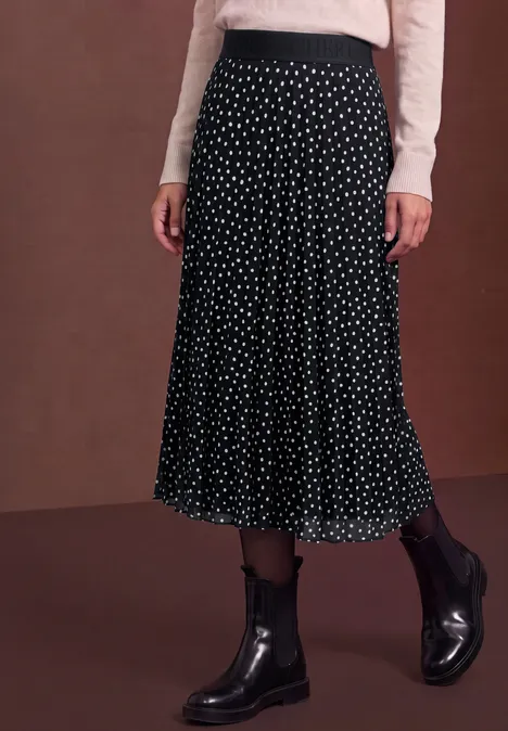 Schwarzer Midirock mit weißen Punkten, kombiniert mit cremefarbenem Oberteil und schwarzen Stiefeletten.