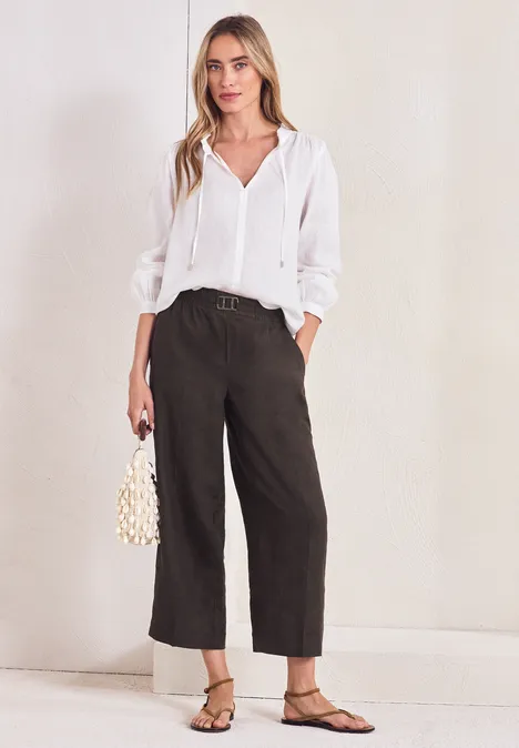 Vrouw in witte blouse, zwarte wijde broek, platte sandalen en klein pareltasje.