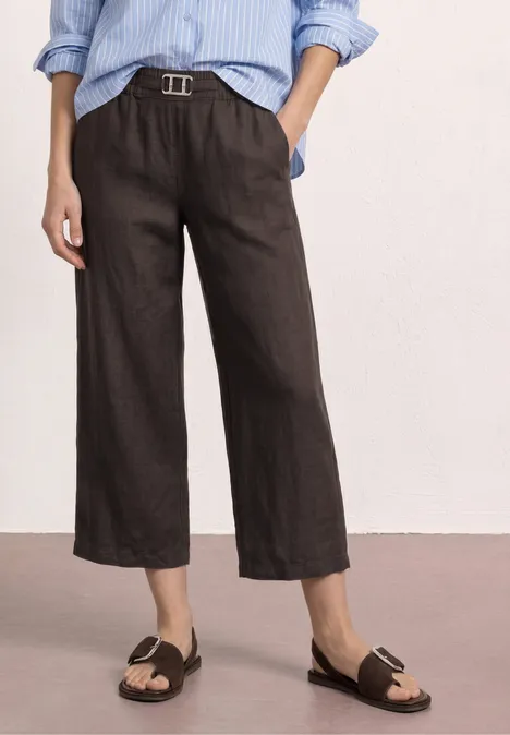 Dames wijde, enkellange zwarte linnenbroek met lichtblauw gestreept overhemd, riem en sandalen.