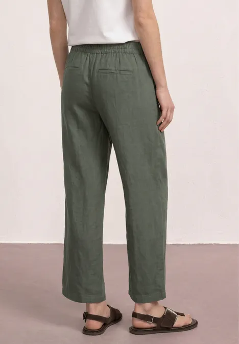 Achteraanzicht van een persoon met losse kaki linnen broek, wit topje en sandalen.