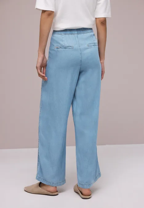 Achteraanzicht van een persoon in wijde lichtblauwe jeans, een witte top en beige sloffen.