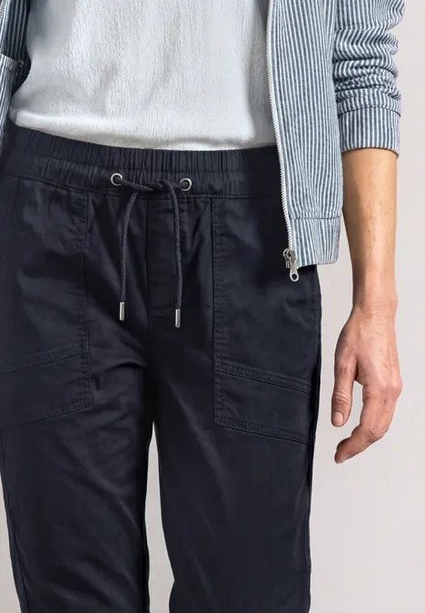 Person trägt dunkelblaue Jogginghose mit Kordelzug, weißen Pullover und hellblaue Strickjacke.