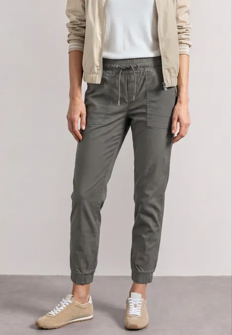 Femme portant chemise blanche, veste claire, pantalon de jogging olive et baskets beiges.