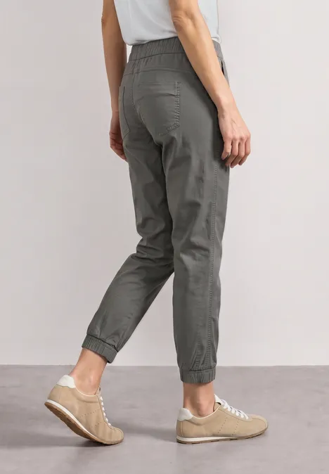 Personne vue de dos portant un pantalon gris resserré aux chevilles et des baskets beiges.