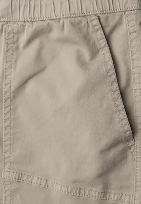 Close-up van een beige broekzak met elastische tailleband en zichtbare stiksels.