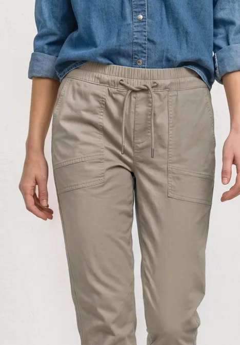 Een persoon draagt een comfortabele beige cargobroek van licht materiaal met zijzakken.
