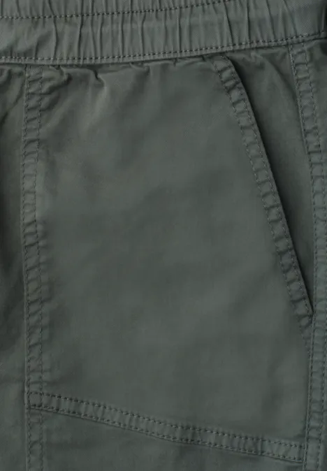 Close-up van een donkergroene broek met elastische taille en zijzak.