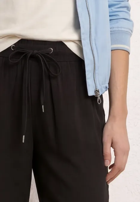 Close-up van persoon in zwarte joggingsbroek en lichtblauw jack.