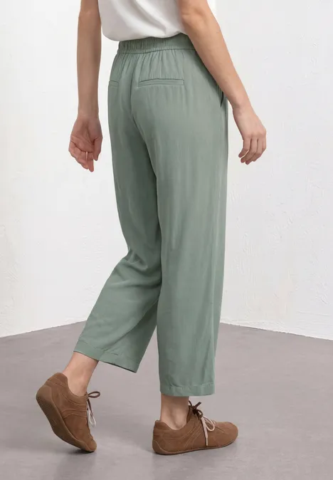 Eine Person trägt locker sitzende, grüne, knöchellange Hose mit elastischem Bund und braune Schnürschuhe.