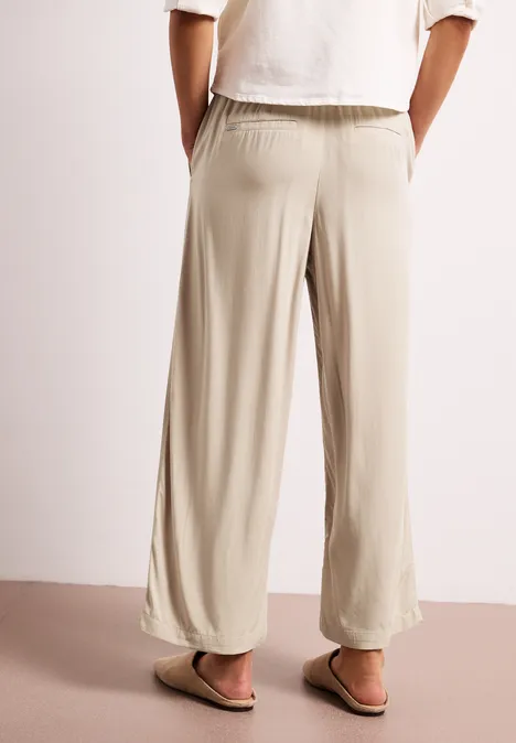 Lichtbeige, wijdvallende broek met elastische taille, losvallende pijpen en subtiele zoom, gecombineerd met sandalen.