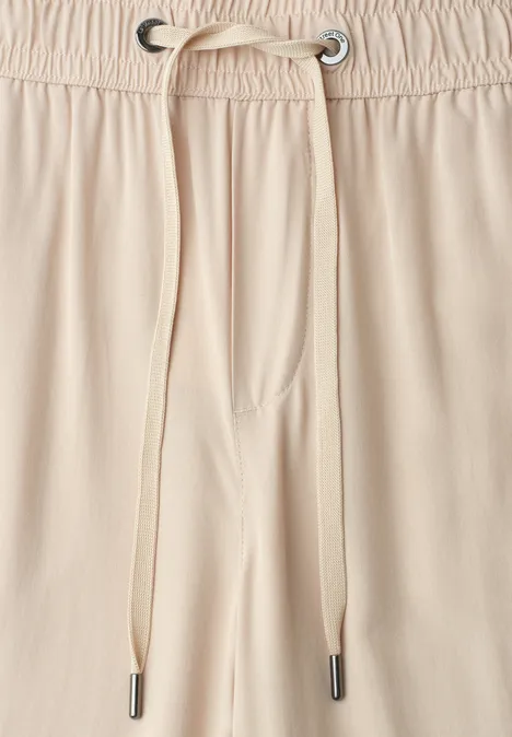 Close-up van een beige broekband met elastische tailleband en koord met metalen oogjes.