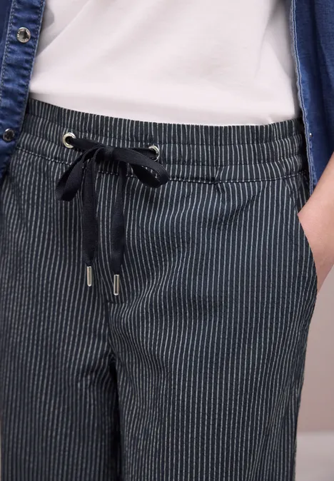 Close-up van een donkerblauwe, gestreepte broek met aantrekkoord en hand in de zak.