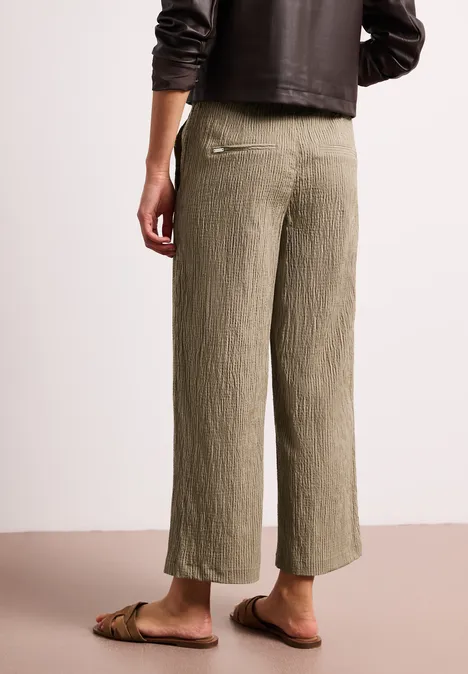 Achteraanzicht van een persoon in losse, geplooide kaki culottebroek en platte sandalen.