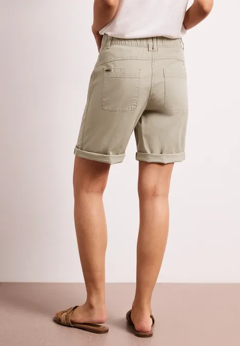 Achteraanzicht van persoon in kaki opgerolde shorts en slippers, lichte achtergrond.