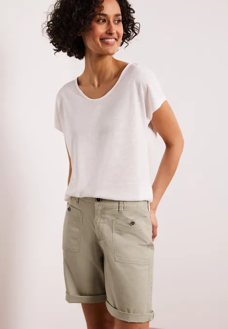 Een persoon draagt een eenvoudig wit T-shirt en beige bermudashort met omslag en zakken.