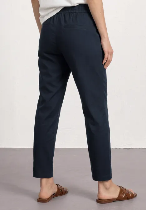 Slim Leg Chino mit Elastikbund shadowed navy Frau trägt dunkelblaue knöchellange Hose mit elastischem Bund und braunen Slippern.