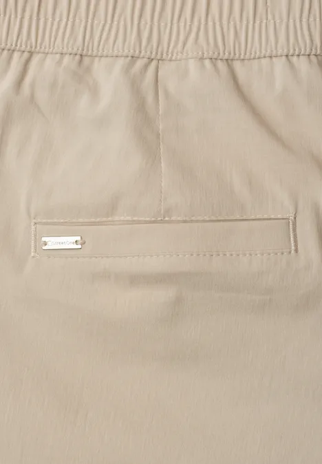 Beige Hose mit elastischem Bund und schmales Paspeltasche mit Metall-Label.