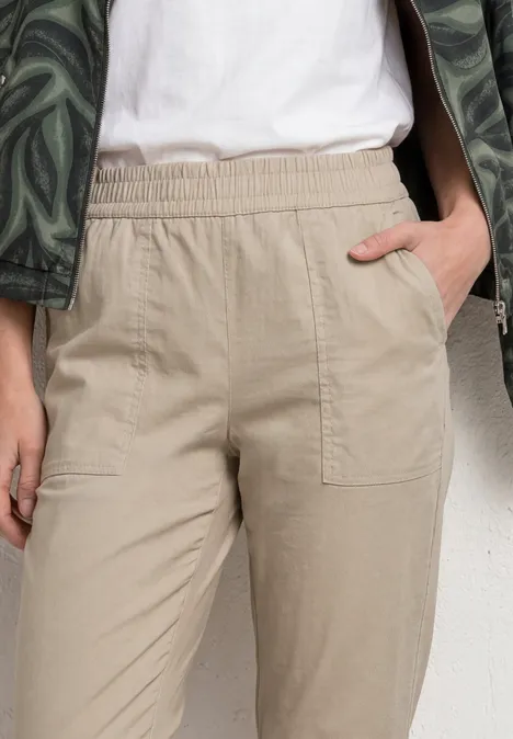 Beige Hose mit Gummibund und aufgesetzten Taschen, Hand steckt lässig in der Tasche.