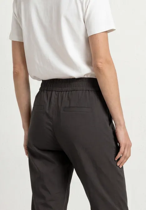 Slim Leg Chino mit Elastikbund deep earth Rückenansicht einer Person in weißem T-Shirt und schwarzer Hose mit elastischem Bund und Gesäßtasche.