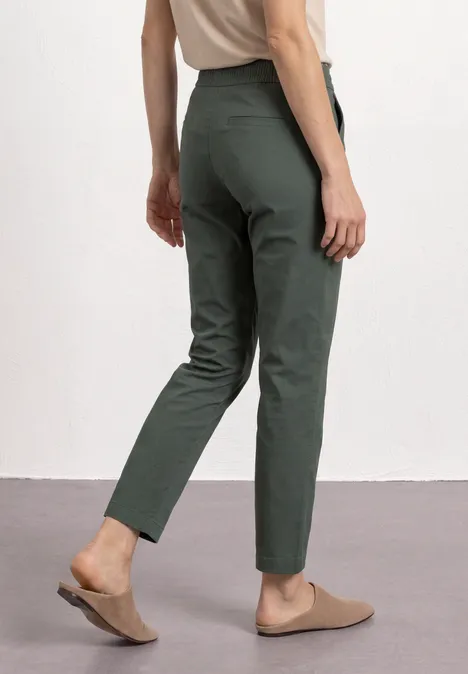 Eine Person trägt grüne, schmale Hose und bequeme braune Mules.