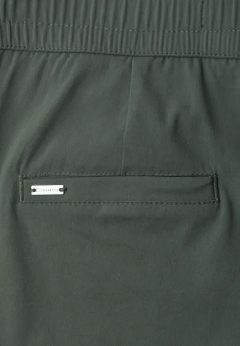 Dunkelgrüne Stoffhose mit elastischem Bund und einer aufgesetzten Gesäßtasche mit Metallplakette.