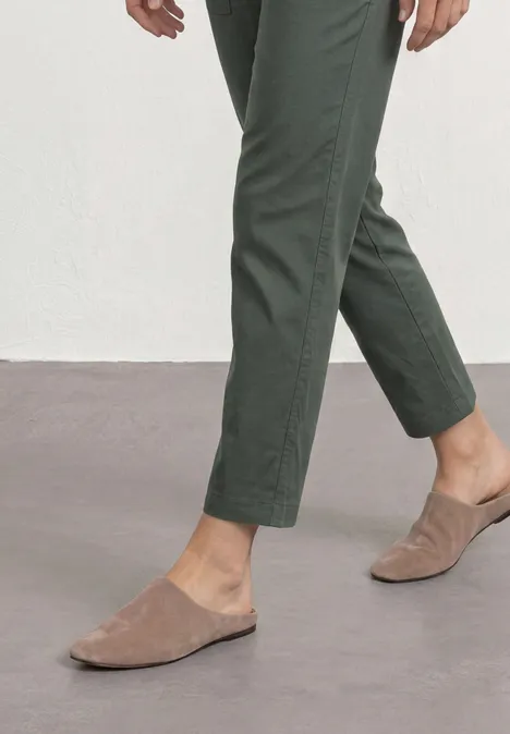 Beine in grünen Hosen und beigen Wildleder-Slippern auf grauem Boden
