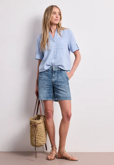 Frau mit hellblauer Bluse, Jeansrock, Sandalen und Korbtasche.