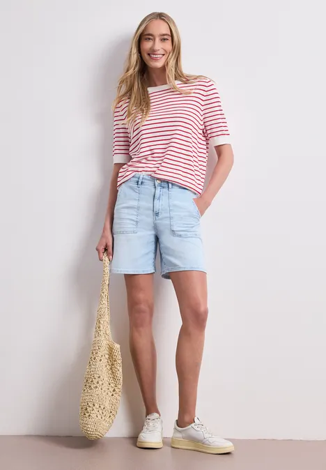 Straight Leg Shorts im Casual Fit bleached light blue wash Frau in rot-weiß gestreiftem T-Shirt, hellblauen Jeans-Shorts, Makramee-Tasche und weißen Sneakern.
