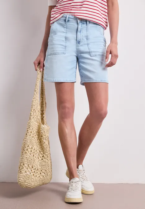 Straight Leg Shorts im Casual Fit bleached light blue wash Frau in hellblauen Jeansshorts, gestreiftem Shirt, weißen Sneakern und Häkel-Tasche.