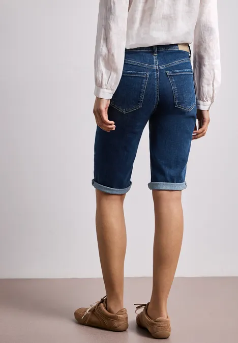 Frau von hinten in blauer Jeans-Bermuda, weißer Bluse und braunen Loafers.