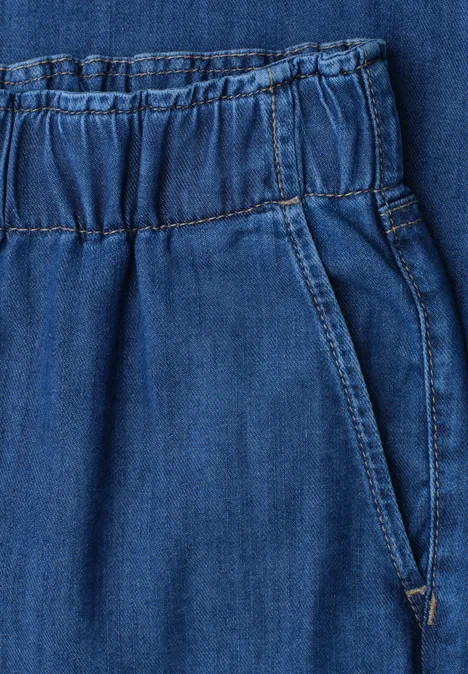 Close-up van een blauwe spijkerbroek met elastische taille en zijzak.