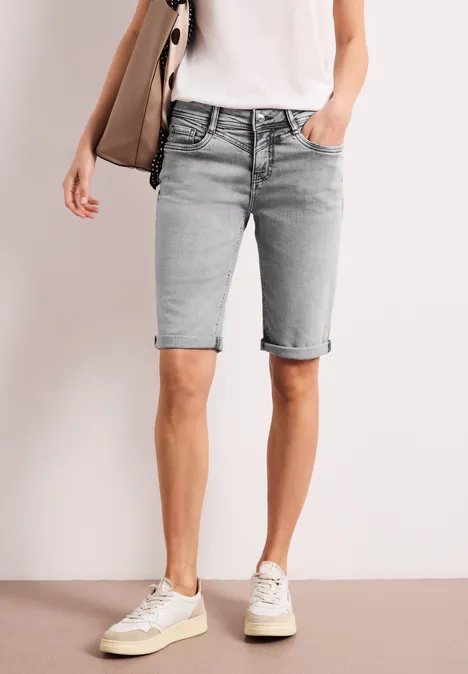 Een persoon draagt lichtgrijze, knielange denim shorts met omgeslagen zoom, gecombineerd met wit T-shirt en sneakers.