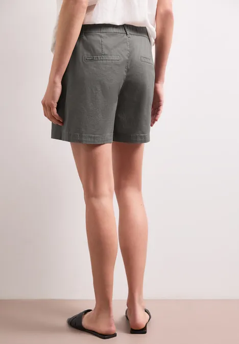 Achteraanzicht van een persoon in grijze shorts en zwarte sandalen tegen neutrale achtergrond.