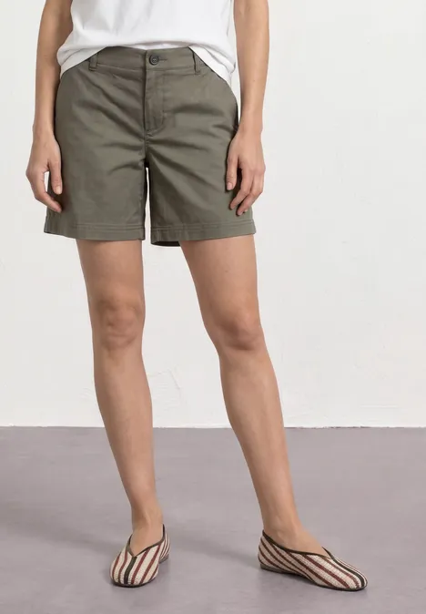 Mid Waist Chino Shorts im Casual Fit dusky green Frau trägt khakifarbene Shorts, weißes Top und schwarz-weiße flache Sandalen.