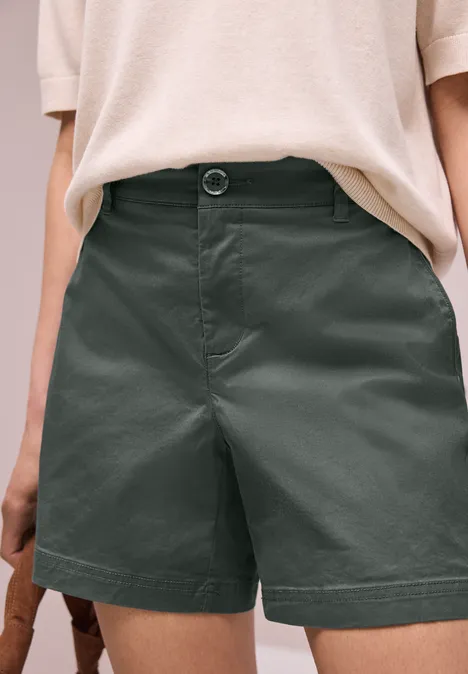 Dunkelgrüne, knielange Shorts mit hohem Bund, kombiniert mit lockerem, hellbeigem T-Shirt.