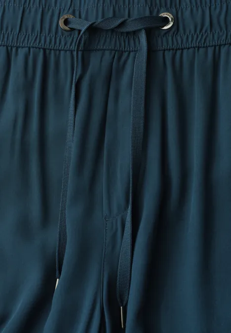 Close-up van een donkergroene broek met elastische tailleband en trekkoord.