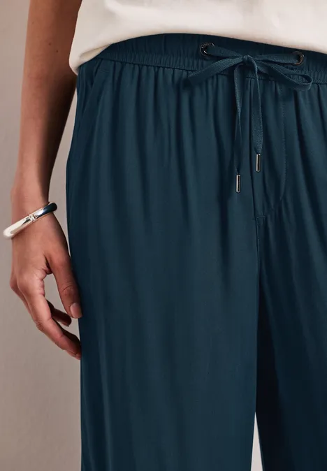 Vrouw met wijde donkerblauwe broek met trekkoord, wit shirt en armbanden om haar pols.