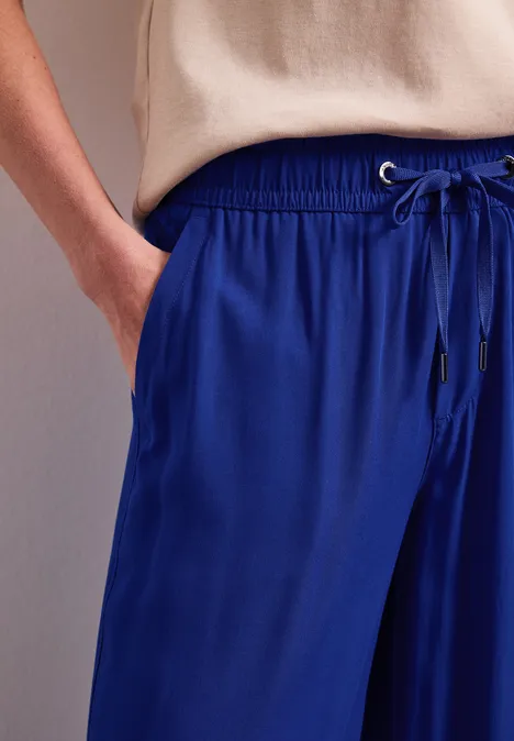 Close-up van een persoon in losse blauwe broek met trekkoord, hand in de zak.