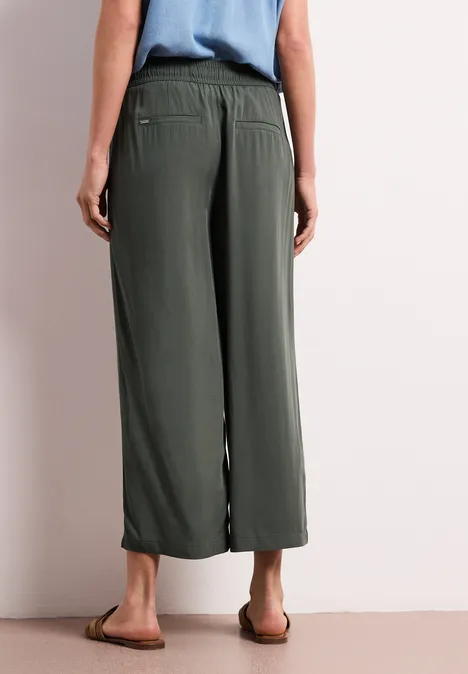 Achteraanzicht van een persoon met olijfgroene, wijde culottebroek en platte sandalen.