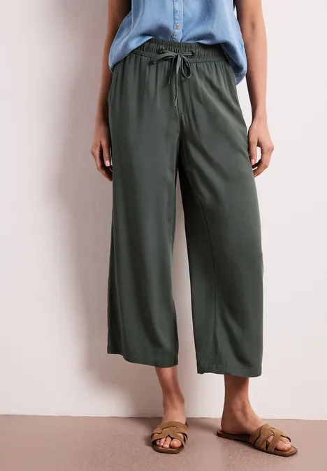 Vrouw draagt wijde groene broek met trekkoord en platte sandalen.