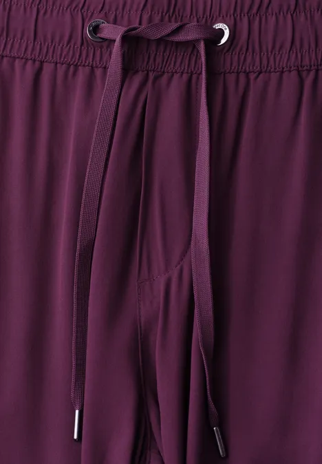 Close-up van de taille van een bordeauxrode broek met elastische band en aantrekkoord.